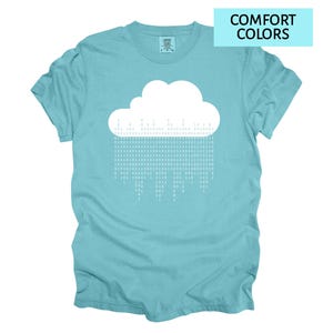 Pode incluir: Camiseta azul claro com um desenho de nuvem branca e chuva de c&oacute;digo bin&aacute;rio. A camiseta tem as palavras "COMFORT COLORS" em um ret&acirc;ngulo azul claro no canto superior direito. Gola redonda.