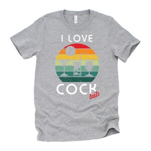 Op de afbeelding: Een grijs T-shirt met een vintage-stijl grafische afbeelding van een zonsondergang met drie cocktailglazen. De tekst "I LOVE COCKtails" is op het T-shirt gedrukt.