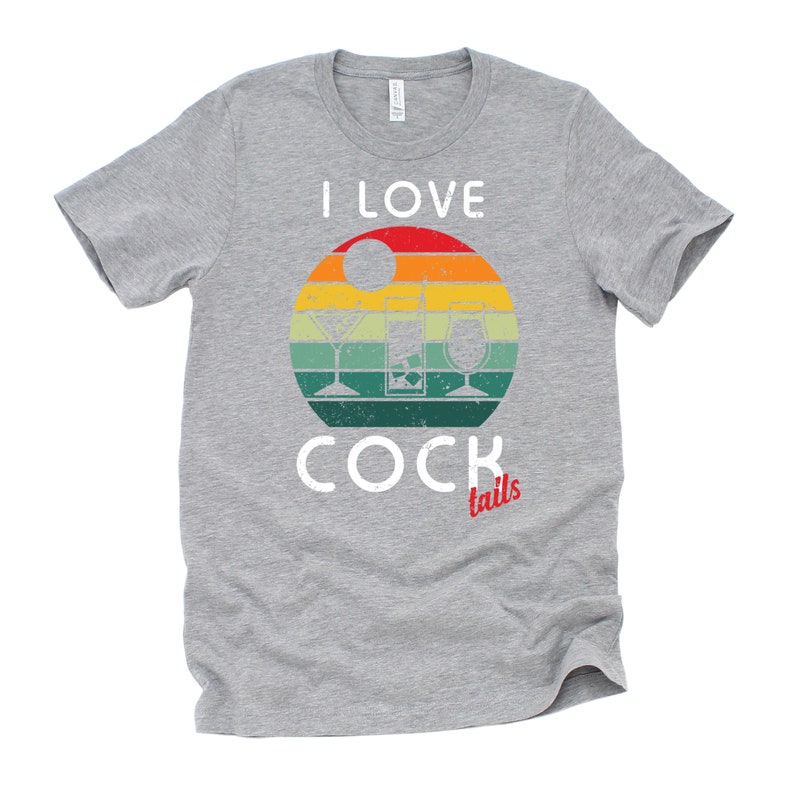Op de afbeelding: Een grijs T-shirt met een vintage-stijl grafische afbeelding van een zonsondergang met drie cocktailglazen. De tekst "I LOVE COCKtails" is op het T-shirt gedrukt.