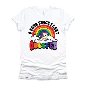 May include: White t-shirt with a colorful graphic. The design features a rainbow, clouds, and a cartoon cat. Text on the shirt reads "0 days since I last QUEEFED."