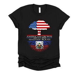 May include: Black t-shirt with a tree design. The tree trunk is the Haitian flag and the treetop is the American flag. The text reads "American Grown with Haitian Roots".