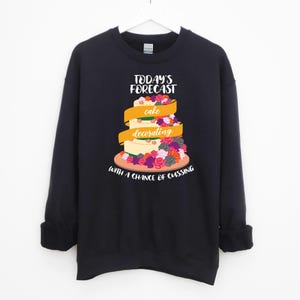 May include: Black sweatshirt with a humorous graphic of a cake with the text "Today's Forecast: Cake Decorating with a Chance of Cussing".