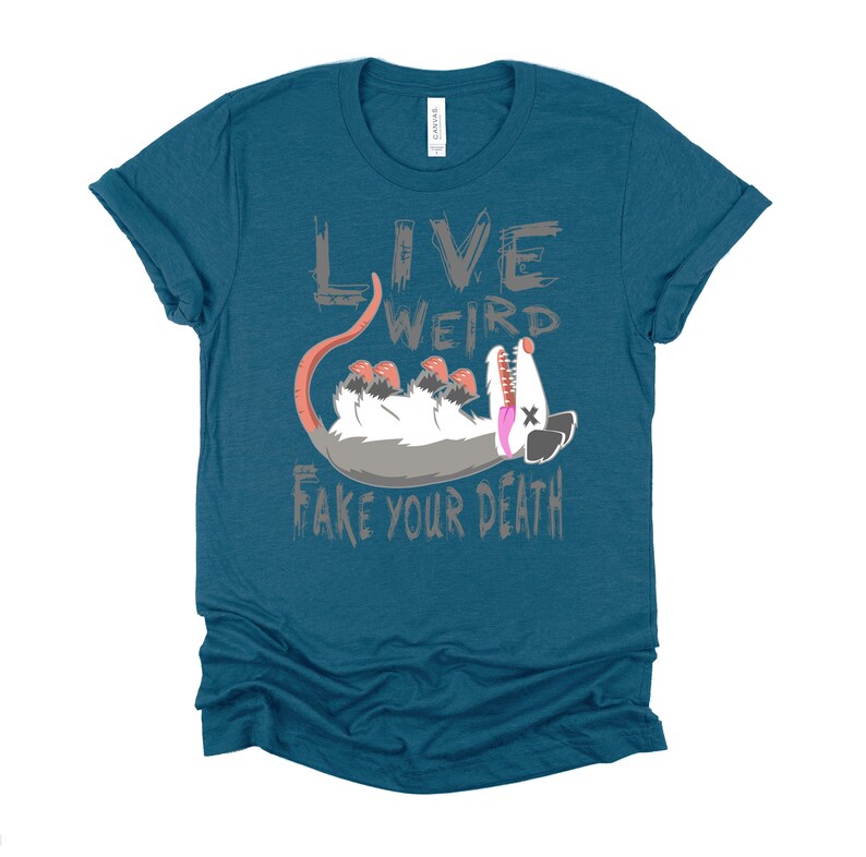 Op de afbeelding: Tealblauwe T-shirt met een grijze afbeelding van een opossum met de tekst "Live Weird Fake Your Death".