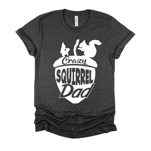 May include: A dark gray t-shirt with a white acorn design. The acorn has two squirrels inside and the text "Crazy Squirrel Dad" written on it.