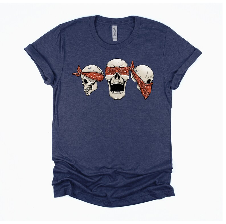 May include: A navy blue t-shirt with a graphic of three skulls wearing red bandanas. The skulls are blindfolded with the bandanas.