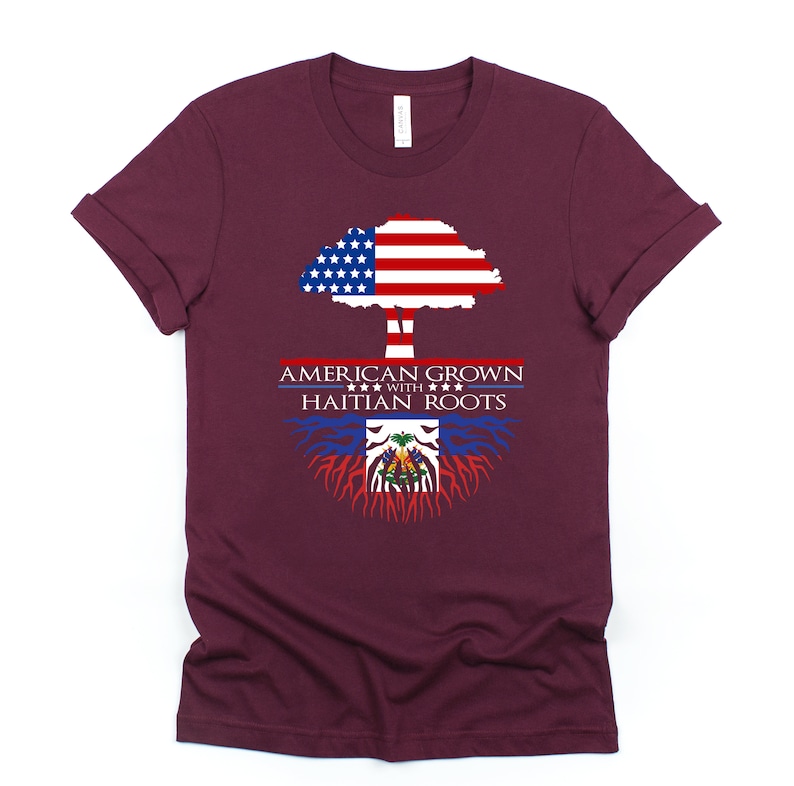 May include: A maroon t-shirt with a tree design. The tree is made up of the American flag and has roots made up of the Haitian flag. The text "AMERICAN GROWN WITH HAITIAN ROOTS" is printed on the shirt.
