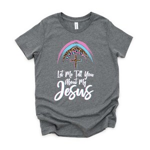 May include: A gray t-shirt with a rainbow design featuring a cross and leopard print. The text "Let Me Tell You About My Jesus" is printed on the shirt.