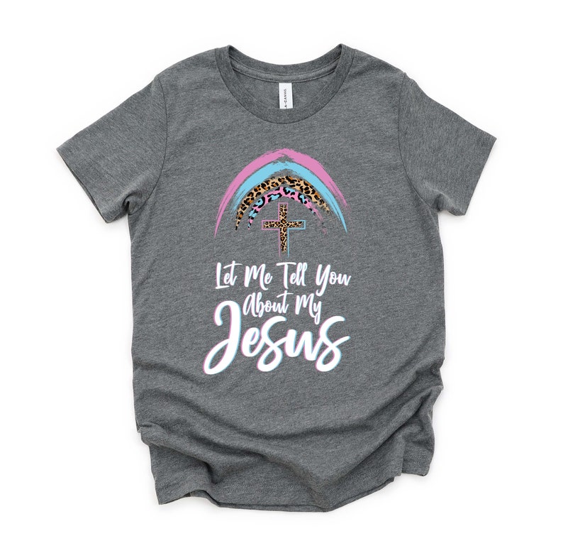 May include: A gray t-shirt with a rainbow design featuring a cross and leopard print. The text "Let Me Tell You About My Jesus" is printed on the shirt.