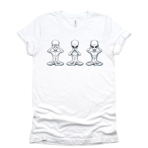 May include: White t-shirt featuring a graphic of three grey aliens in a row, each with their hands covering their eyes, mouth, and ears, respectively. The aliens are seated with their legs crossed.