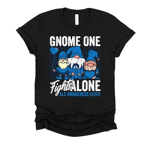 May include: Black t-shirt with a graphic of three gnomes wearing blue hats and holding blue ribbons. The text "Gnome One Fights Alone" and "ALS Awareness" is printed on the shirt.