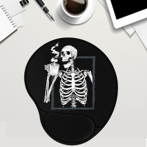 May include: Black round mouse pad featuring a white skeleton illustration holding a cup of coffee. The skeleton is framed in a grey rectangle.