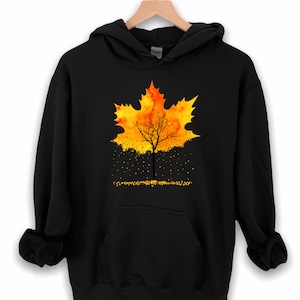 May include: Black hoodie with a graphic of a yellow and orange watercolor maple leaf with a tree trunk in the center. The leaves are falling from the tree.
