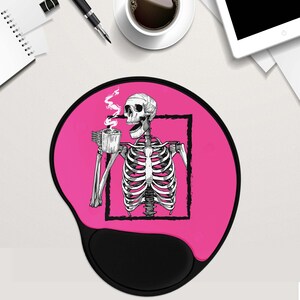May include: Pink round mouse mat with a black skeleton drinking coffee. The skeleton is inside a black square frame. The mouse mat has a black, round, raised area for the mouse.