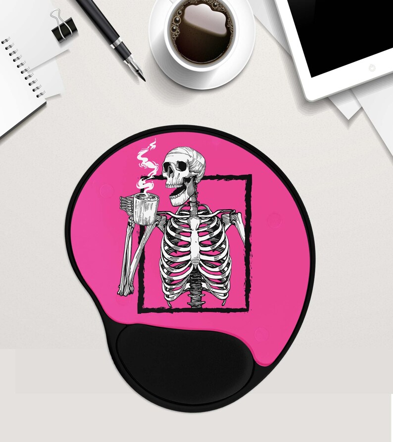 May include: Pink round mouse mat with a black skeleton drinking coffee. The skeleton is inside a black square frame. The mouse mat has a black, round, raised area for the mouse.