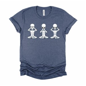 May include: A navy blue t-shirt featuring a graphic of three grey aliens in a see no evil, hear no evil, speak no evil pose.
