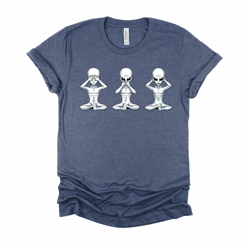 May include: A navy blue t-shirt featuring a graphic of three grey aliens in a see no evil, hear no evil, speak no evil pose.