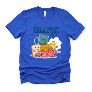 May include: A royal blue t-shirt featuring a graphic of breakfast foods with faces. The text "The Breakfast Club" is printed on the shirt.