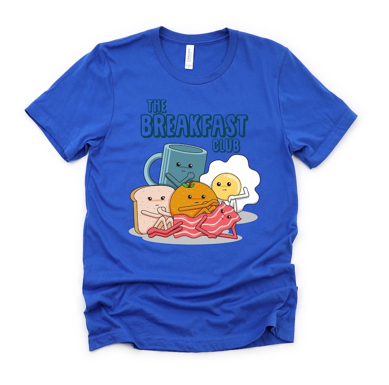 May include: A royal blue t-shirt featuring a graphic of breakfast foods with faces. The text "The Breakfast Club" is printed on the shirt.