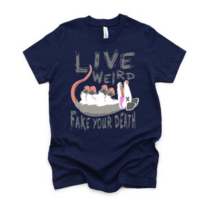 Op de afbeelding: Donkerblauw T-shirt met een grijze opossum-afbeelding en de tekst "Live Weird Fake Your Death".