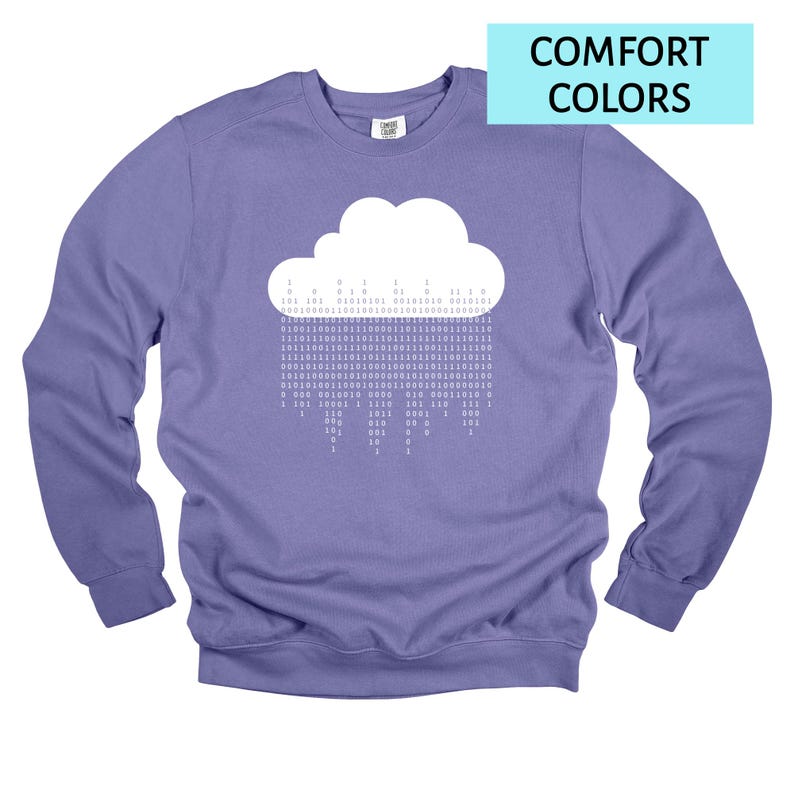 Op de afbeelding: Een lila sweatshirt met een witte wolkengrafiek met binaire code die 'regent'. De tekst "COMFORT COLORS" staat in een lichtblauwe rechthoek. De sweatshirt heeft een ronde hals en lange mouwen.