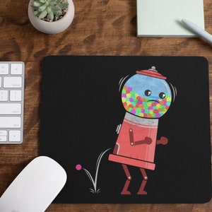 May include: Black mousepad featuring a cartoon gumball machine with a sad face, filled with colorful gumballs. The gumball machine is red with a blue top and is bouncing a pink ball. A white keyboard and mouse are visible.