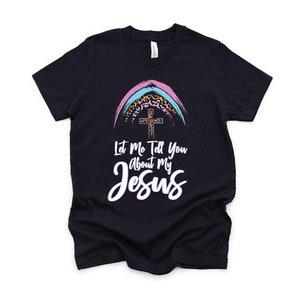 May include: A black t-shirt with a rainbow design featuring a cross and leopard print. The text "Let Me Tell You About My Jesus" is printed on the shirt.