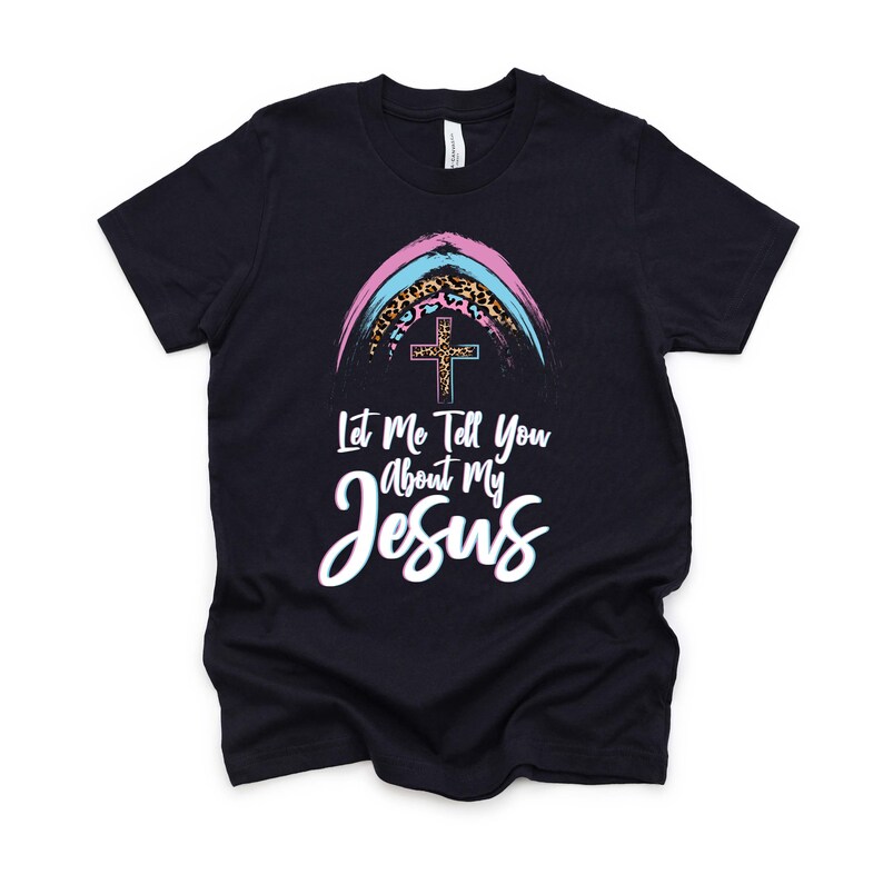May include: A black t-shirt with a rainbow design featuring a cross and leopard print. The text "Let Me Tell You About My Jesus" is printed on the shirt.