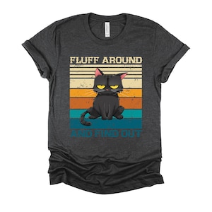 May include: A dark gray t-shirt with a vintage-style graphic of a black cat with a grumpy expression. The graphic says "Fluff Around And Find Out".
