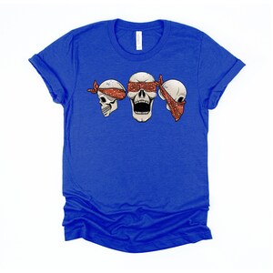 May include: A royal blue t-shirt with a graphic of three skulls wearing red bandanas. The skull in the middle has its eyes covered by the bandana.