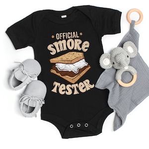 May include: Black baby onesie with a graphic of a s'more and the text "OFFICIAL SMORE TESTER".