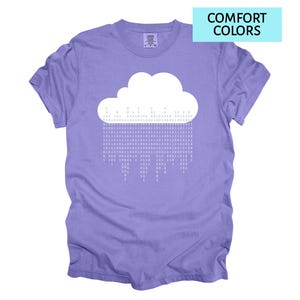 Pode incluir: Uma camiseta lil&aacute;s com um desenho de nuvem branca e c&oacute;digo bin&aacute;rio representando chuva. A camiseta tem gola redonda e mangas curtas. O texto "COMFORT COLORS" est&aacute; em um ret&acirc;ngulo azul claro no canto superior direito.