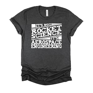 May include: Dark heather grey t-shirt with white text that reads "It's not rocket science it's aerospace engineering".