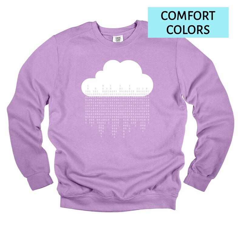 Op de afbeelding: Een lila sweatshirt met een witte wolkengrafiek en binaire code regen. De tekst "COMFORT COLORS" staat in een lichtblauwe rechthoek rechtsboven. De trui heeft een ronde hals en lange mouwen.