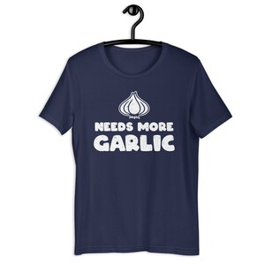 May include: A navy blue t-shirt with a white graphic of a garlic clove and the text "Needs More Garlic".