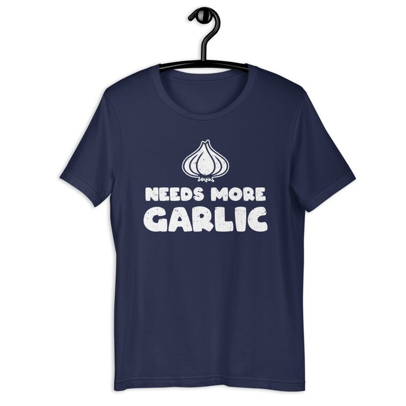 May include: A navy blue t-shirt with a white graphic of a garlic clove and the text "Needs More Garlic".