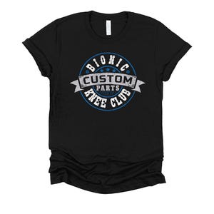 May include: Black t-shirt with a distressed graphic. The graphic is a circular design with the words "BIONIC CUSTOM PARTS KNEE CLUB" in white and blue. The shirt is made of a soft material.