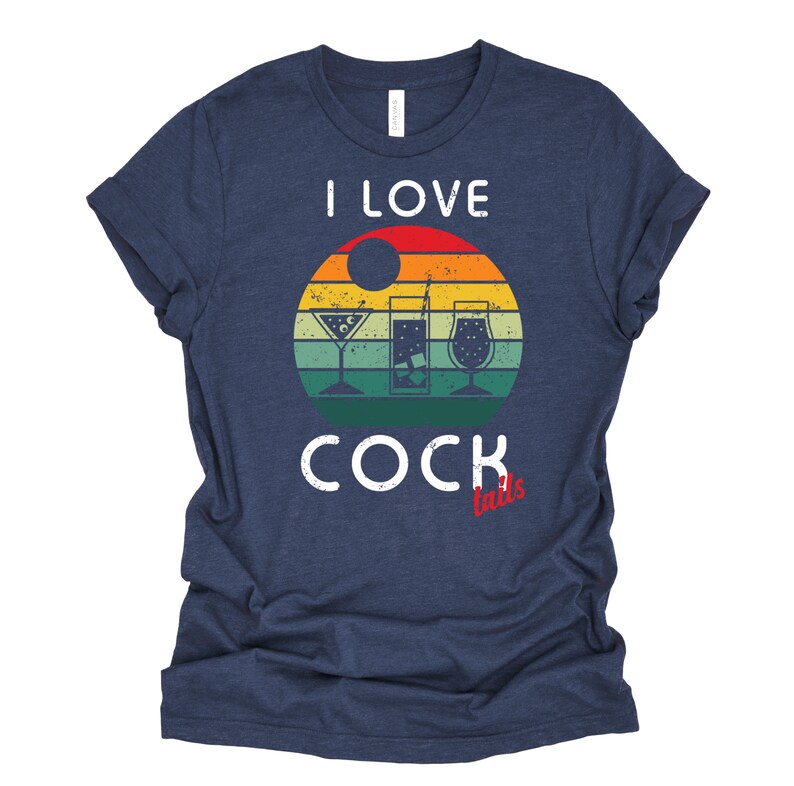 Op de afbeelding: Een marineblauw t-shirt met een vintage-stijl grafische afbeelding met de tekst "Ik hou van cocktails" met een zonsondergang achtergrond en drie cocktailglazen.