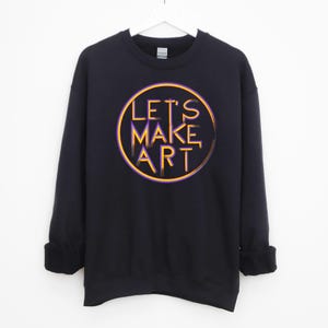 May include: Black sweatshirt with a circular graphic design featuring the text "LET'S MAKE ART" in yellow and purple.