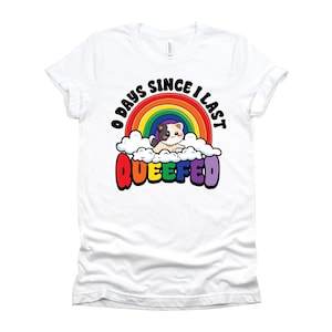 May include: A white short-sleeve t-shirt featuring a graphic of a small cat sitting on white clouds in front of a rainbow. The text above the rainbow reads 0 DAYS SINCE I LAST and the text below the clouds reads QUEEFED in bold colorful letters.