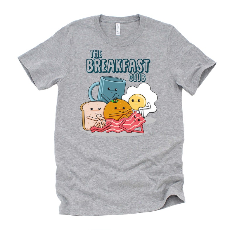 May include: A heather grey t-shirt featuring a cartoon illustration of breakfast foods. The text "The Breakfast Club" is printed on the shirt.