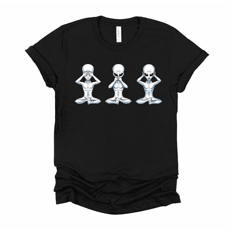 May include: Black t-shirt featuring a graphic of three grey aliens in a row. The aliens are seated with their hands covering their eyes, ears, and mouth. The graphic is a play on the "See no evil, hear no evil, speak no evil" saying.