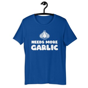 May include: A royal blue t-shirt with a white graphic of a garlic clove and the text "Needs More Garlic".