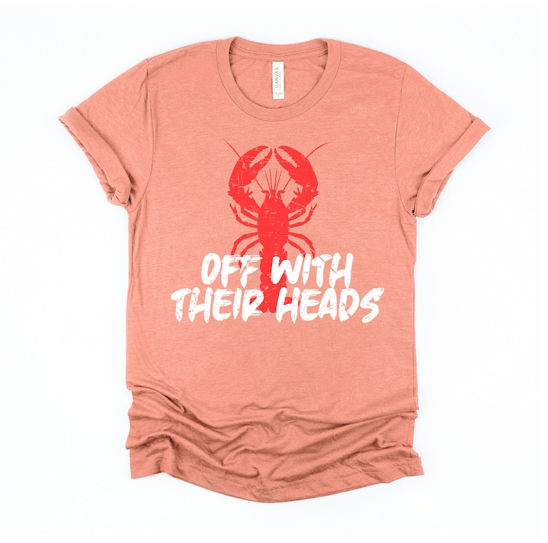 K&ouml;nnte beinhalten: Ein korallenfarbenes T-Shirt mit einem roten Hummer-Motiv und dem Text "Off with their heads" in Wei&szlig;.