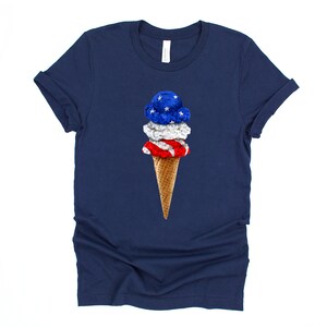 May include: A navy blue t-shirt with a graphic of an ice cream cone with red, white, and blue ice cream. The ice cream is decorated with stars and stripes.