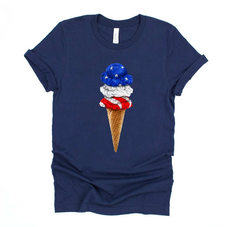 May include: A navy blue t-shirt with a graphic of an ice cream cone with red, white, and blue ice cream. The ice cream is decorated with stars and stripes.