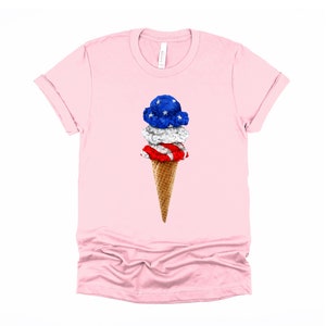 May include: A pink t-shirt with a graphic of an ice cream cone with three scoops of ice cream. The ice cream is decorated with the colors of the American flag: red, white, and blue.