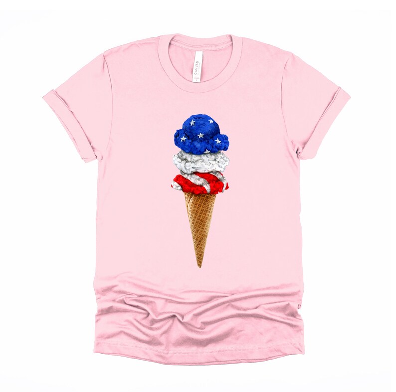 May include: A pink t-shirt with a graphic of an ice cream cone with three scoops of ice cream. The ice cream is decorated with the colors of the American flag: red, white, and blue.