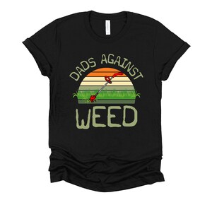 May include: Black t-shirt with a retro sunset graphic and the text "Dads Against Weed" with a weed trimmer in the middle of the graphic.