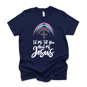 May include: A navy blue t-shirt with a rainbow and cross graphic. The text "Let Me Tell You About My Jesus" is printed on the shirt.
