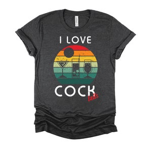 Op de afbeelding: Een donkergrijs T-shirt met een vintage-zonnenonderganggrafiek en de tekst "Ik hou van cocktails" in wit. Het woord "cocktails" is in rood.